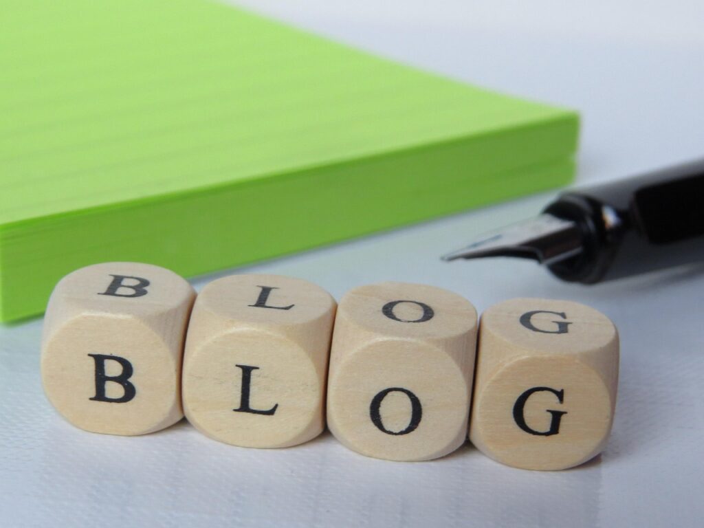 Wooden letter blocks spelling BLOG beside a notepad and pen